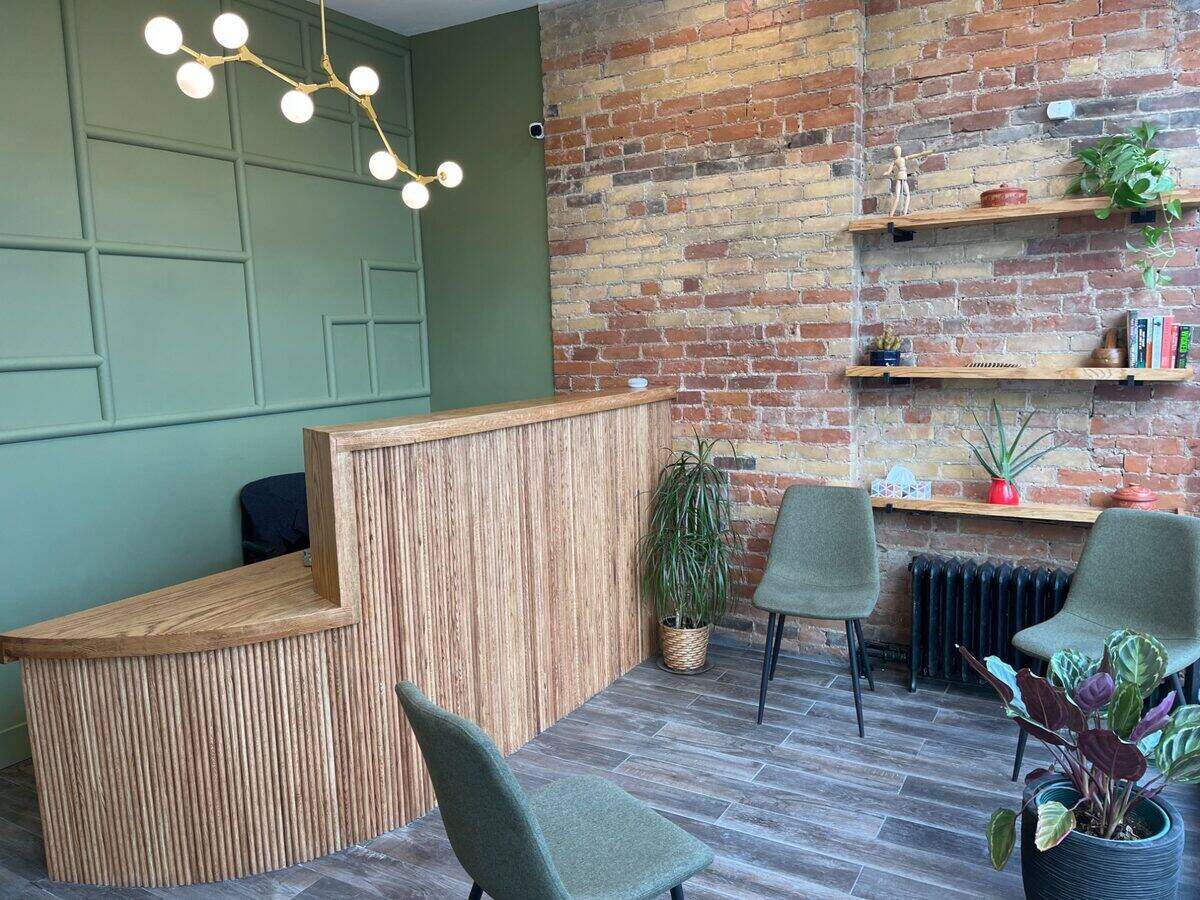 The Healing Theory clinic reception area with green accent wall, exposed brick, and warm wood reception desk